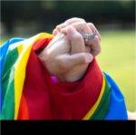 Two folded hands draped with a rainbow pride flag.